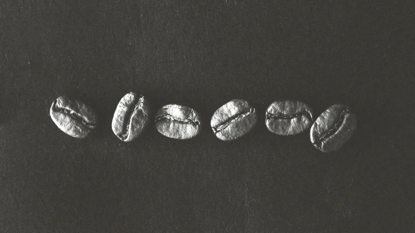 Seis granos de café tostado en fila sobre fondo oscuro, en blanco y negro