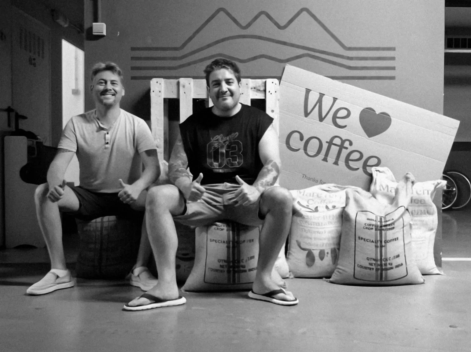 Los dos fundadores sentados sobre sacos de café, con un cartel We love coffee